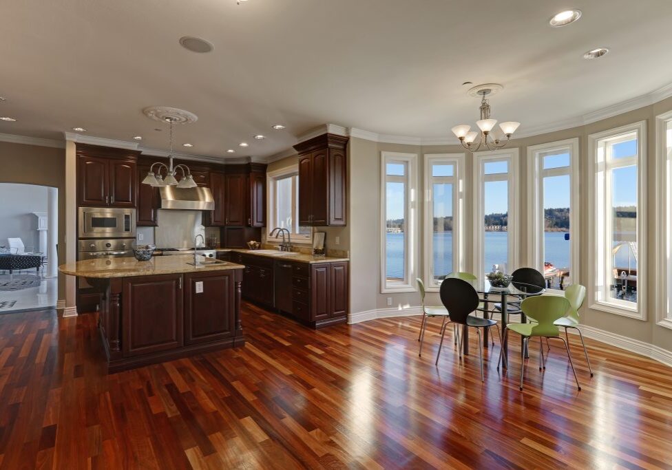 Open floor plan interior of luxury waterfront home: Warm and inviting kitchen connected with sun filled breakfast nook boasts polished hardwood floors. Northwest USA